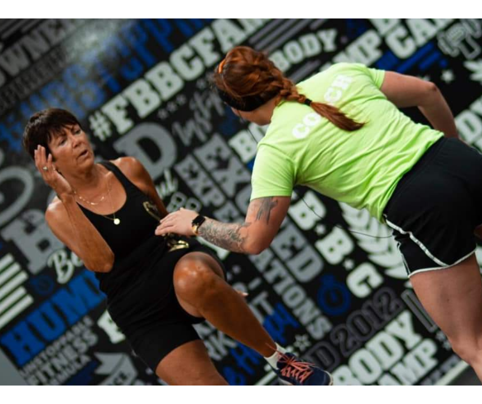 Coach helping a member with form in front of the Fit Body Boot Camp wall